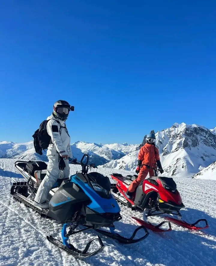 Two travellers with snowmobiles on a snowy mountain