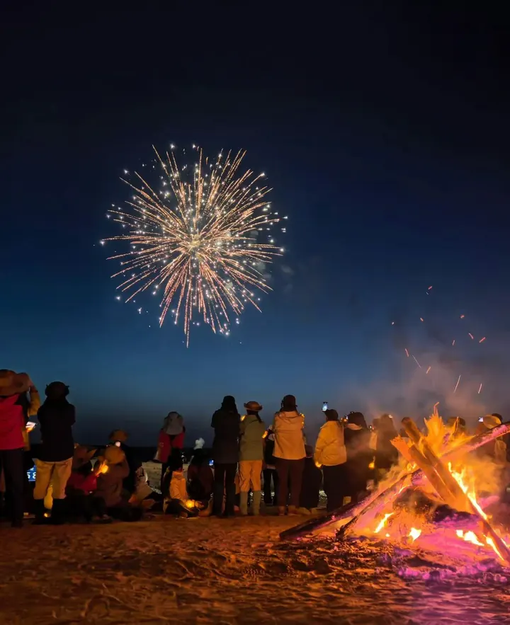 Travellers watching fireworks beside a winter campfire